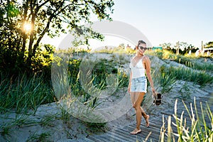 Summer vibes! Cool young woman enjoying life. Happy pretty girl walking on beach boardwalk at sunset. Perfect hot weekend.