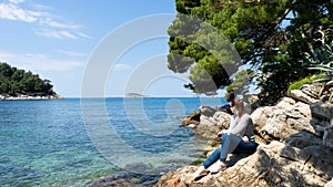 Summer vibes girl portrait. Young pretty woman looking on the adriatic sea, sitting on cliff. Travel concept. Red head pony tail