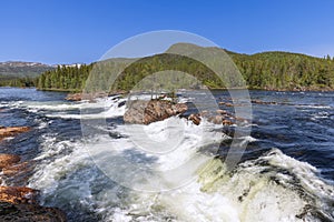 A summer view of the Namsen River in Namsskogan, Trondelag, Norway, with cascading waters over large boulders,