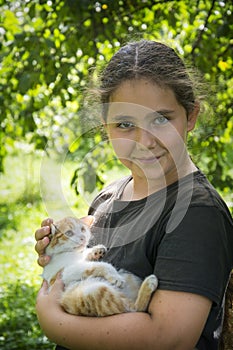 In the summer in the village, a girl holds a white-red little kitten in her arms