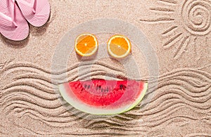 Summer wallpaper, drawing on sand, sea waves and sun, face shape of summer fruits, pink flip-flops, top view, no people