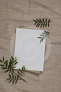 Summer wedding stationery mock-up scene. Blank greeting card, craft paper envelope and green branches on linen textile background