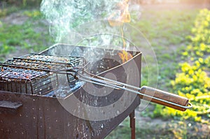 Summer Weekend BBQ Scene On The Backyard. Flaming Charcoal Grill. Grill with fire in nature in the evening