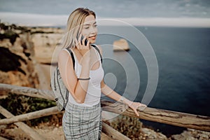 Summer woman using cellphone texting sms message outside. Europe Happy young girl relaxing in sun on mobile phone.