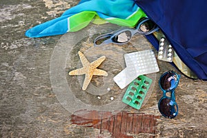 Summer women`s beach accessories for your sea holiday and pill on old wooden background. Concept of medication required in journe