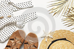 Summer women`s white dress in black peas brown sandals straw hat golden palm leaf shells starfish on light background