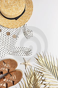 Summer women`s white dress in black peas brown sandals straw hat golden palm leaf shells starfish on light background. Flat lay