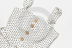 Summer women`s white dress in black peas with natural wooden buttons on light gray background flat lay top view copy