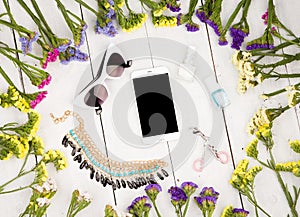 summer women set with colorful flowers around smart phone, sunglasses, cosmetics makeup, bijou and essentials on white wooden