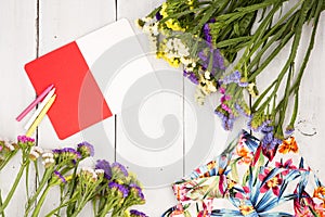 summer women set with dress, colorful flowers, notepad and pencils on white wooden background