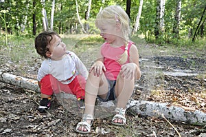 Summer in the woods on birch logs sits two little sisters