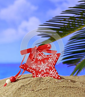 Summer xmas holidays concept. Christmas ornament on sandy beach with palm tree, blue sea and sky background