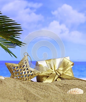 Summer xmas holidays concept. Christmas ornament on sandy beach with palm tree, blue sea and sky background