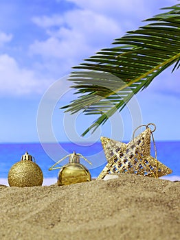 Summer xmas holidays concept. Christmas ornaments on sandy beach with palm tree, blue sea and sky background