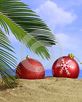Summer xmas holidays concept. Christmas ornaments on sandy beach with palm tree, blue sea and sky background