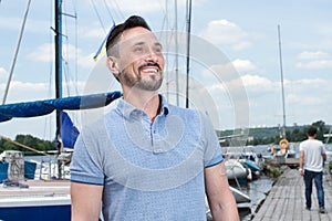 Summer Young cheerful bearded man relaxing on sailboat posing and looking at far on background of boats sky and folded wings