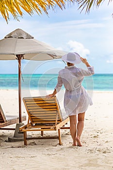 Young woman relaxing at tropical beach during summer vacation, white dress hat, beach shore, umbrella and chairs