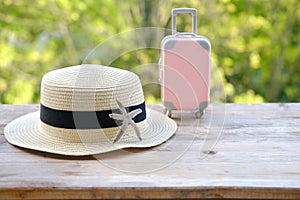 summerhat, suitcase, starfish on old wooden table in garden, beautiful blurred natural landscape in background with green foliage