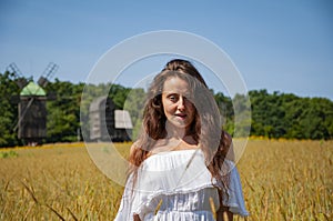 Summertime agronomy. Woman in white dress at Ukrainian field of wheat. Woman in Ukraine field with spikelet. Summer woman in dress