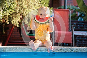 Summertime. Cute baby girl eating watermelon sitting by the pool. Slice of watermelon like a smile. Concept of