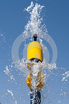 Summertime fun for the kids at the splash pad to play yellow fountain spraying water to bright blue sky portrait view