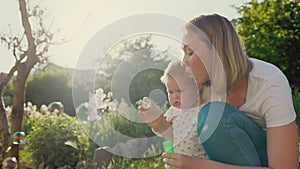 Summertime. Happy young mother hugs her little baby girl and blows soap bubbles. Slow motion. Happy Children's Day