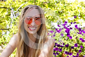 Summertime holidays. Close-up woman happy face in pink sunglasses at garden background. Summer fun weekend. Beautiful girl
