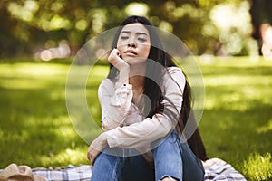 Summertime Sadness. Portrait Of Thoughtful Asian Woman Sitting On Plaid In Park