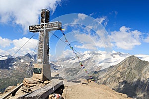 Summit cross and prayer flag on mountain Kreuzspitze with glacier panorama and Grossvenediger, Hohe Tauern Alps, Austria