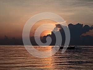 The sun arise behind the cloud over the horizon with floating fishing boat on sea background.