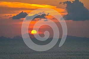 Sun ball hides behind clouds dramatic and colorful sunset over ocean photo