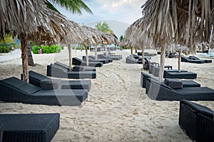 Sun beds/ lounge chairs and straw thatch roof umbrellas on tropical beach