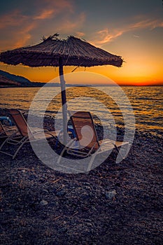 Sun beds on a rocky beach at sunset with a straw umbrella perfect for tourists on the Island of Samothrace in Greece