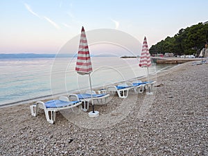 Sun beds and umbrellas on the Podluka beach in the seaside resort of Baska Voda. A beautiful quiet morning by the sea