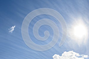 Sun behind long wispy clouds against a blue sky, as a nature background
