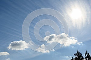 Sun behind long wispy clouds against a blue sky, as a nature background