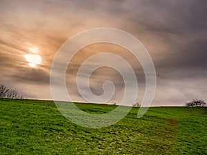 The sun behind the thick clouds, above the grassy hill horizon