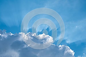 Sun behind a white cloud with blue sky in the background. Sunrays and summer sky