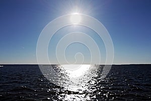 The Sun in the blue sky and the sun glare on the water
