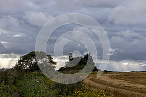 Sun breaking through clouds over lighthouse and wheat field