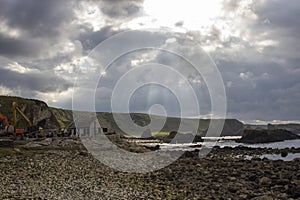 The sun breaks through dark clouds over the harbour at Ballintoy