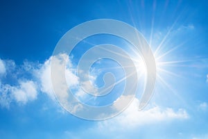 The sun with bright rays in the blue sky with white light clouds.