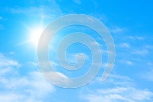 The sun with bright rays in the blue sky with white light clouds