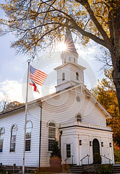Sun burst behind a beautiful white church with an American flag flying high.