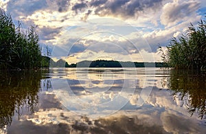 Sun and clouds in the dramatic sky are reflected in the lake. Natural background with clouds and water