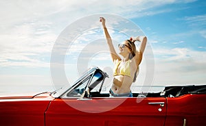 The sun comes out and the top comes down. a happy young woman enjoying a summers road trip.