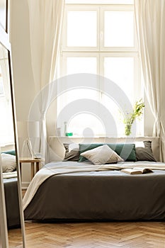 Sun coming through a large window and shinning onto a bed with earth color linen in a wooden floor bedroom interior. Part of the b