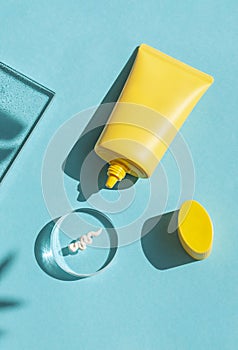 Sun cream yellow tube on the blue background with tropical leaves shadows. Summer vacation cosmetics concept.