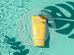 Sun cream yellow tube on the blue water surface with palm leaves shadows. Summer vacation cosmetics concept.