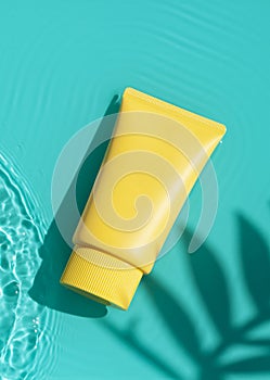 Sun cream yellow tube on the blue water surface with palm leaves shadows. Summer vacation cosmetics concept.